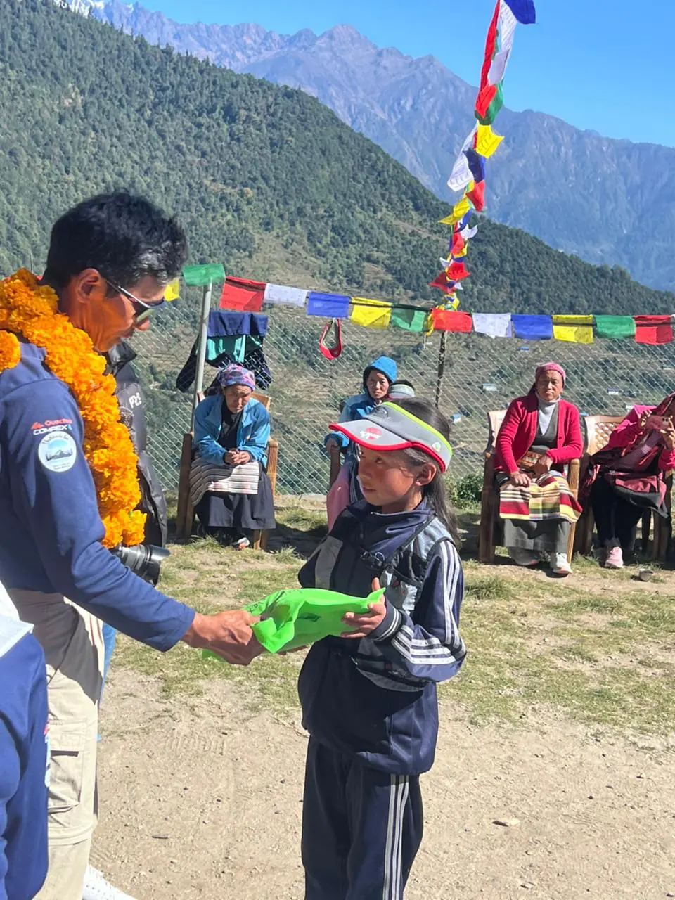 Dawa Dachhiri Sherpa, colliers de fleurs autour du cou, remet une écharpe à un enfant sous les drapeaux de prières