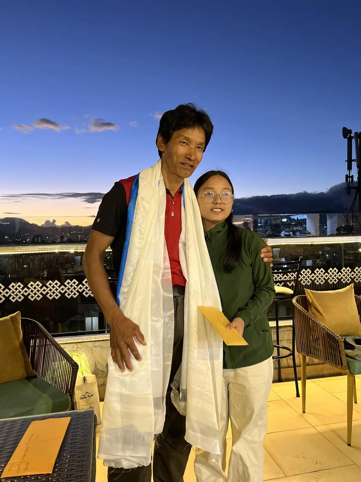 Dawa Dachhiri Sherpa, écharpe blanche autour du cou, aux côtés d'une jeune femme sur une terrasse au coucher du soleil