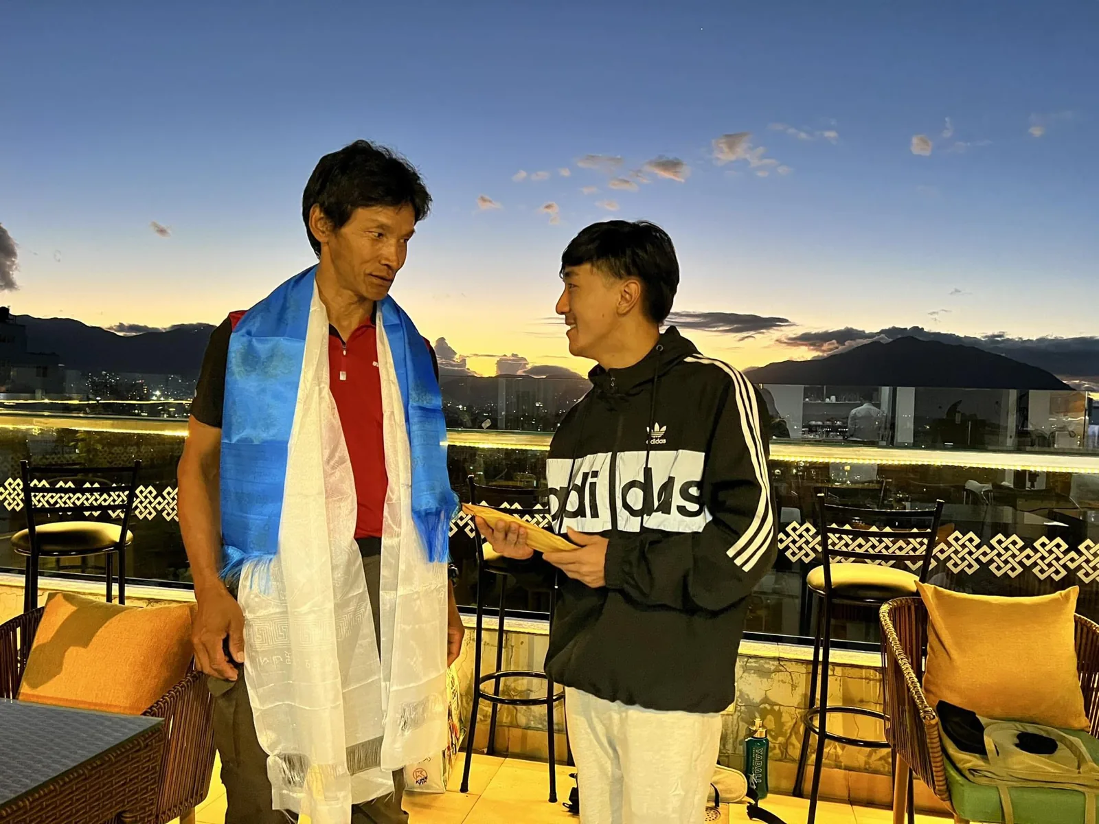 Dawa Dachhiri Sherpa en conversation avec un jeune homme sur une terrasse au crépuscule