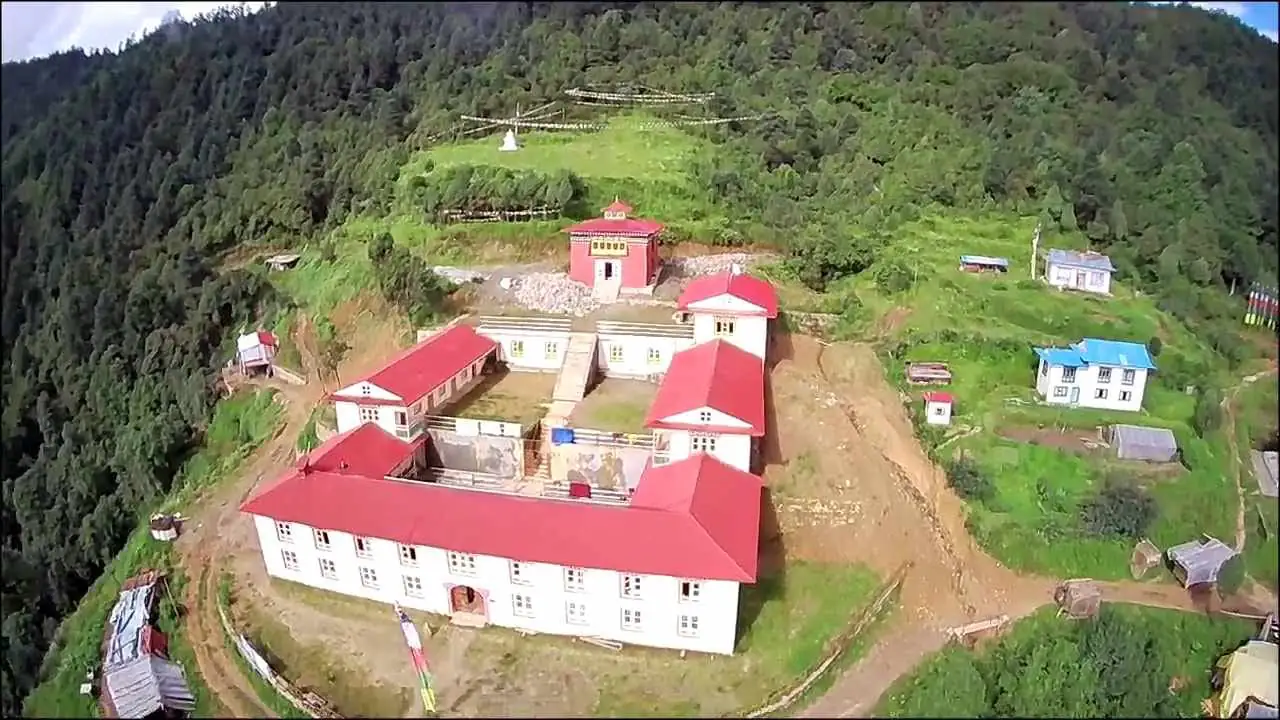Vue aérienne des bâtiments aux toits rouges du monastère, entourés de forêt et de cultures en terrasses