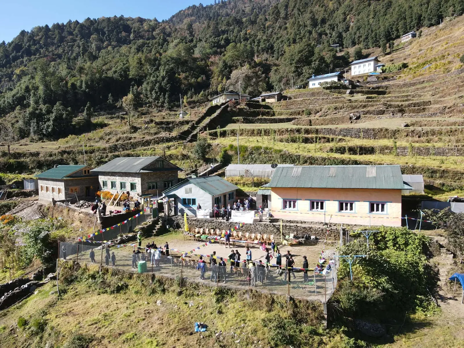 Vue aérienne du village, ses bâtiments et sa cour rassemblant les habitants, à flanc de montagne
